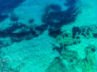 Aerial drone view of transparent sea water at summer. Underwater reefs, sand, rocks and sea grass. Beautiful tropical sea surface, view from above. Sea waves and sun reflection on water surface. 