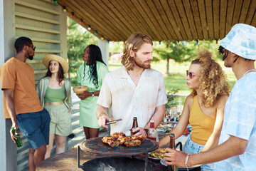 Waist up portrait of young people grilling meat outdoors with friends at barbeque party in Summer