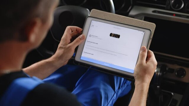 Automotive mechanic running diagnostics software on tablet. Unrecognizable vehicle service manager worker work in mechanics garage, check and maintenance to repair the engine car in workshop