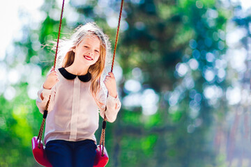 Little smiling girl swinging on a swing outdoors in the park