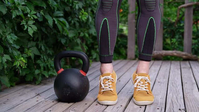 feet and legs of muscular man in compression tights exercising with a heavy iron kettlebell on a wooden backyard deck