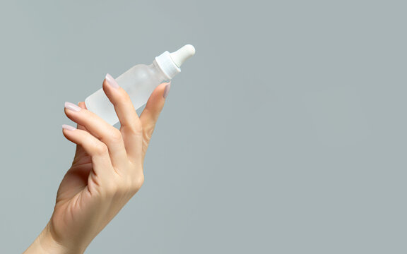Manicured female hand holding up opaque dropper bottle in skincare concept