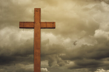 A large cross on a dark cloudy sky background with free space for text