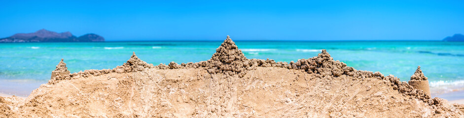 Breites Panorama an einem traumhaft schönen Strand von einer großen Sandburg vor der Brandung des türkisblauen Meeres