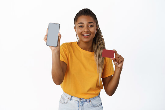 Smiling african american woman showing mobile phone screen and credit card, payment app, money transer and online banking concept, white background