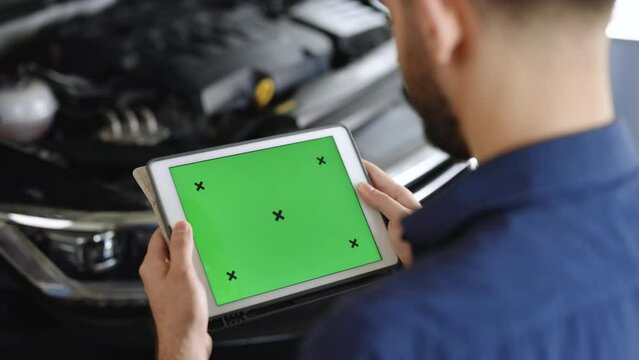 Mechanic running diagnostics software on tablet computer with green screen mockup chromakey. Unrecognizable vehicle service manager worker check and maintenance to repair the engine car in workshop