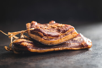 Whole smoked bacon on black table.