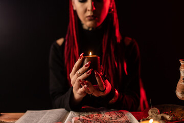 A witch who performs a ritual with a candle. On the table is a spell book and a voodoo doll.