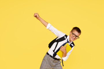 School break. Cheerful mischievous schoolboy in uniform with a backpack jumps on a yellow...