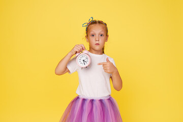 Portrait of a cute girl with a small alarm clock on a yellow background