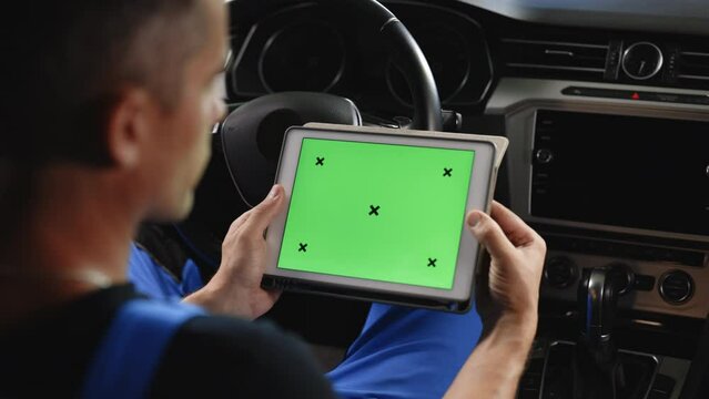 Unrecognizable vehicle service manager worker check and maintenance to repair the engine car in workshop. Mechanic running diagnostics software on tablet computer with green screen mockup chromakey