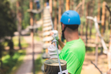 View of high ropes course, process of climbing in amusement acitivity rope park, passing obstacles and zip line on heights in climbing safety equipment gear between the trees, summer sunny day