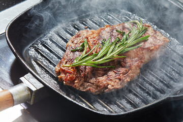 the cook prepares a meat steak on a grill pan close-up, on a dark background