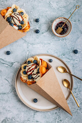 Bubble waffle with ice cream, banana and blueberry in paper cup over gray marble background