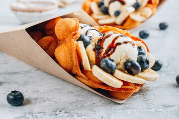 Delicious bubble waffle with ice cream, banana and blueberry on gray marble background.