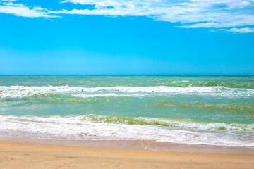 Fototapeta na wymiar Sea with waves and sandy shore, blue sky on the horizon. Travel and tourism