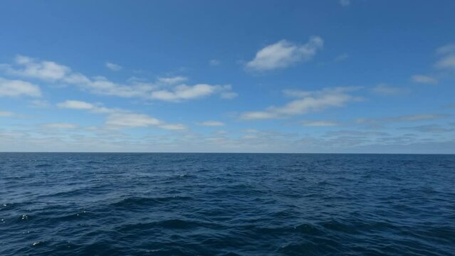 Ocean with Waves and Blue Sky with Clouds a View from A Moving Ship Looking Far at Horizon Line
