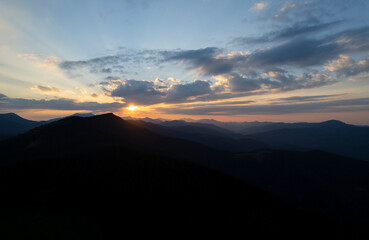 Beautiful evening landscape. Coniferous forest covers mountain hills. Forested hills in rising fog. Mountain sunset hills. Breathtaking aerial view of the tall mountains covered by the forest. 