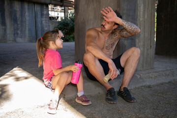 A father and his daughter are resting after a workout.