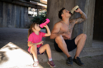 A father and his dauther drinking water after a workout.