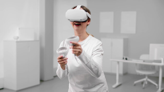 Young woman in white clothes play video game using vr goggles and controllers