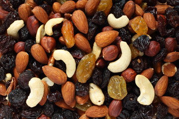 Top view of a pile of large shelled almonds, shelled hazelnuts, cashew nuts, large dark blue raisins and yellow raisins, dried cranberries arranged randomly. Closeup