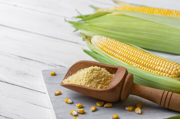 Corn flour in wooden bowl or spoon with fresh corn cobs, kernels on rustic table