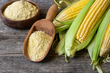 Corn flour in wooden bowl or spoon with fresh corn cobs, kernels on rustic table