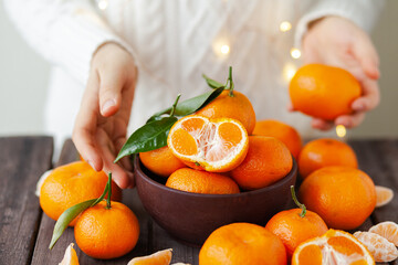 Young girl in white knitted sweater holding fresh ripe tangerines in a bowl on wooden background. Natural source of vitamin C in winter