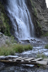 Obraz premium A flowing waterfall behind a small wooden bridge. Selective focus and blurred background. 