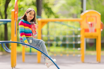 Fototapeta premium Charming smiling little girl, sitting with a plastic bottle of water on the playground