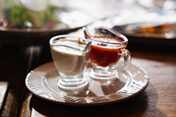 saucepans with white and red sauces in a white plate on a wooden table.