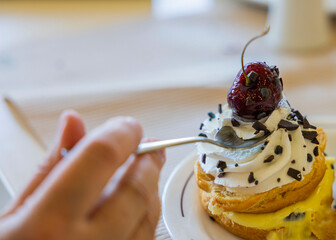 Close up view of female hand with tea spoon taking cherry from top of cake.