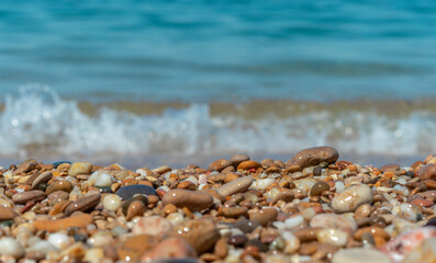 Pebble beach with wet pebbles. Against the backdrop of sea foam and sea waves. Low Angle View. Close-up, selective focus, blurred foreground, blurred background