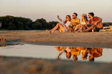 Group of friends having fun on beach, taking selfies and smiling