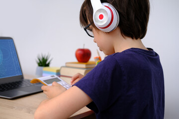 smart child, boy 9-10 years, primary school student in glasses and headphones calculates...