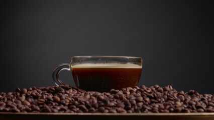 Fragrant coffee drops falling in espresso cup close up. Mug standing on seeds.