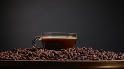 Full coffee cup standing on pile grains close up. Drops falling down on drink.