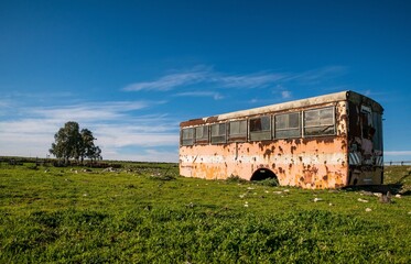 Beautiful view of an old abandoned bus in a green field under cloudy sky