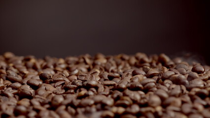 Closeup roasted coffee seeds background. Fragrant seeds pouring down on roaster.