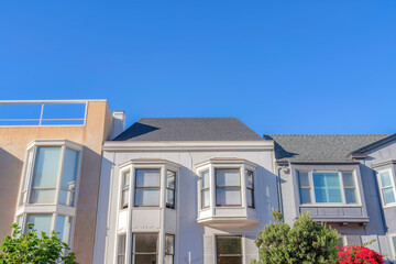 Facade of adjacent houses with bay windows against the blue sky at San Francisco, CA