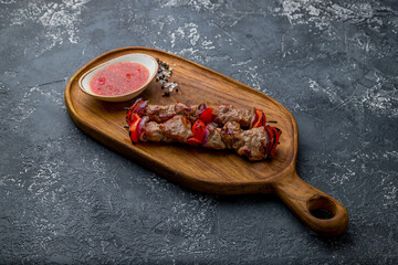 Kebab of veal on the board with tomato sauce on dark stone table