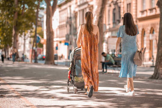 Fototapeta Two young women walking in the streets of Zagreb, Croatia and pushing a pram with a small kid in front of them. Young mother strolling with a kid on a sunny day.