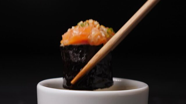 Dip one sushi rolls in soy sauce on black background. Closeup