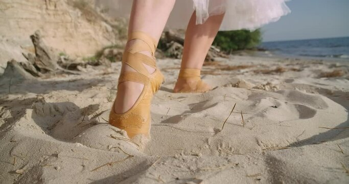 Slim female foot in yellow pointies drawing circle in slow motion on sandy beach. Unrecognizable Caucasian ballerina in tutu standing in sunshine on river bank or sea shore. Cinema 4k ProRes HQ