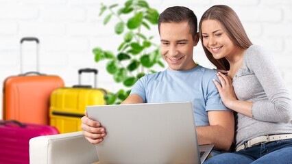 Excited tourists couple booking hotel room online, using laptop, with suitcases ready for vacation trip