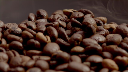 Aromatic steam lying coffee grains closeup. Smoke coming over roasted seeds.