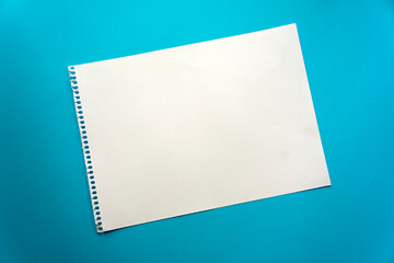 Blank sheet of paper space for design and lettering on a beautiful blue background. A sheet of perforated paper torn from a notepad rests obliquely on the surface. Square sheet of paper