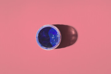 one jar of blue gouache paint on a colored background, top view
