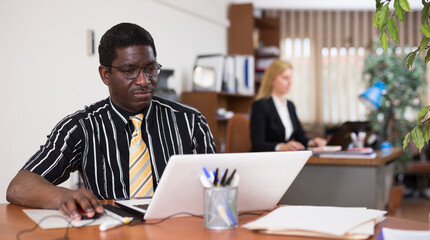 Fototapeta premium Portrait of focused african american man working at office desk. Daily work routine and responsibilities concept